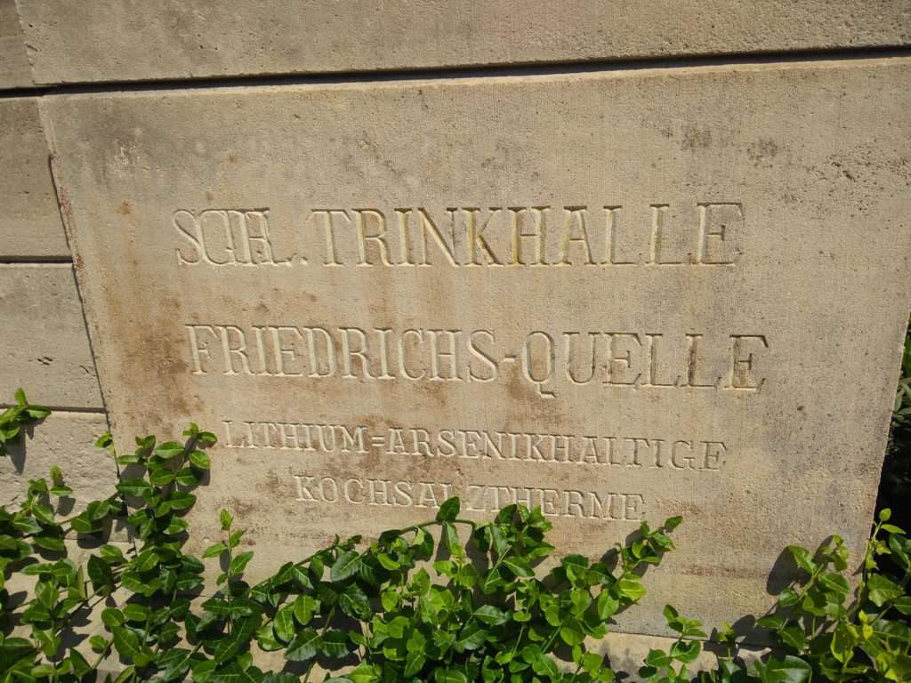 An engraving on the side of the Trinkhalle that reads in German, ""Lithium- and Arsenic-containing saline thermal spa."