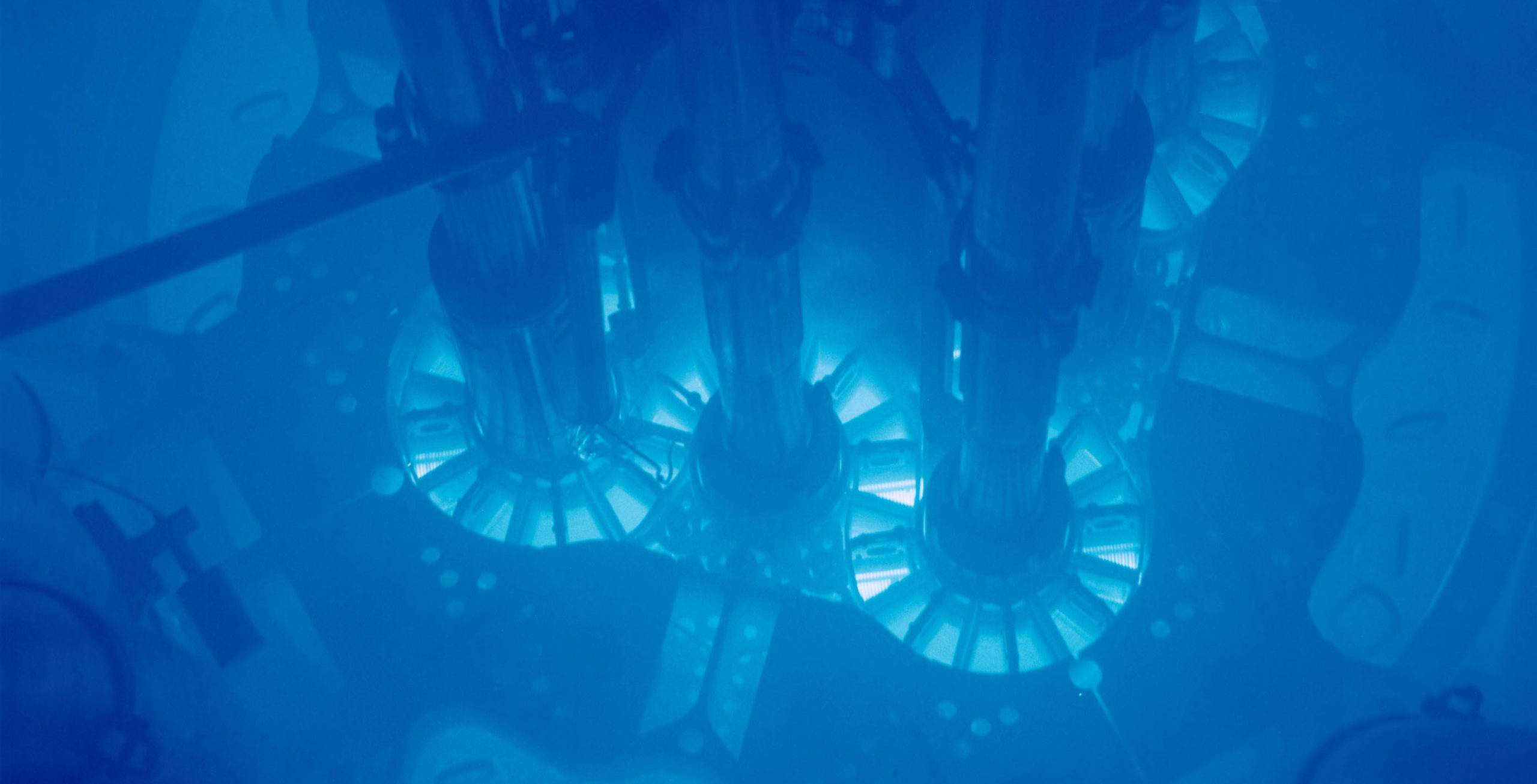 Nuclear fuel plates submerged in water, showing the blue light of Cherenkov radiation.